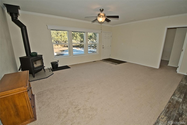 living room featuring ceiling fan, a wood stove, crown molding, and carpet floors