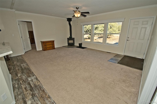 unfurnished living room featuring ceiling fan, carpet, crown molding, and a wood stove