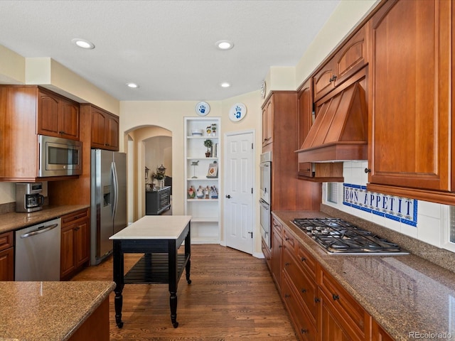 5700 S Benton Cir, Littleton, CO 80123 - kitchen featuring appliances with stainless steel finishes, premium range hood, dark wood finished floors, arched walkways, and dark stone countertops