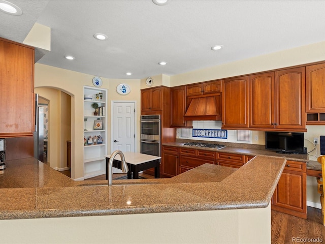 5700 S Benton Cir, Littleton, CO 80123 - kitchen featuring stainless steel appliances, custom exhaust hood, arched walkways, built in shelves, and stone countertops
