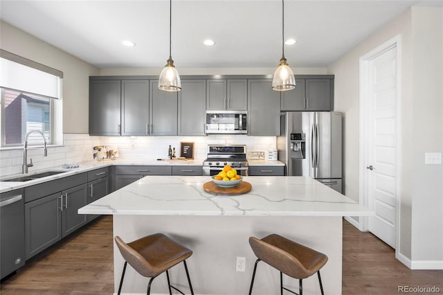 kitchen with light stone countertops, a breakfast bar area, a sink, gray cabinetry, and stainless steel appliances