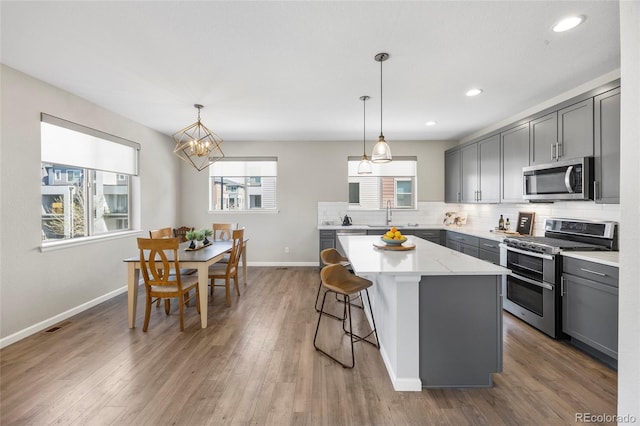 kitchen featuring a kitchen island, gray cabinetry, baseboards, and appliances with stainless steel finishes