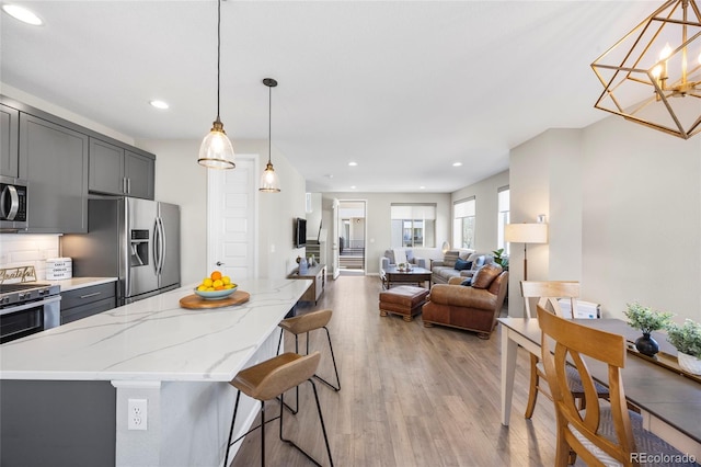 kitchen featuring light stone countertops, appliances with stainless steel finishes, gray cabinets, light wood-style flooring, and tasteful backsplash