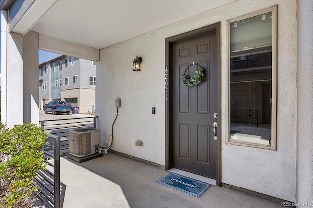 property entrance with covered porch, central AC unit, and stucco siding