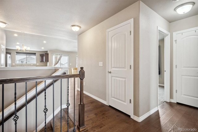 hallway featuring dark wood-type flooring, a textured ceiling, and a notable chandelier