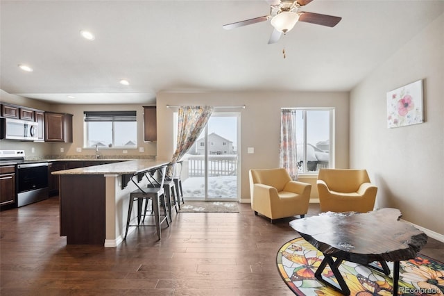 kitchen with dark brown cabinetry, stainless steel electric range, dark hardwood / wood-style floors, and a breakfast bar area