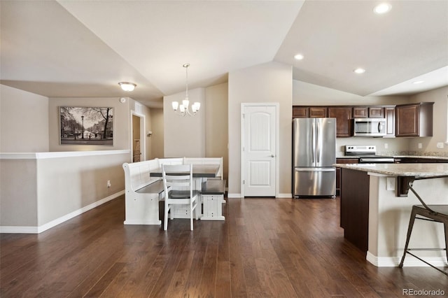 kitchen featuring stainless steel appliances, a kitchen breakfast bar, hanging light fixtures, lofted ceiling, and dark wood-type flooring