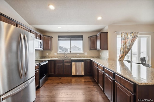 kitchen with stainless steel appliances, kitchen peninsula, sink, dark hardwood / wood-style floors, and light stone countertops