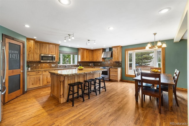 10380 W Warren Ave, Lakewood, CO 80227 - kitchen with stainless steel appliances, wall chimney exhaust hood, light wood-style floors, a breakfast bar area, and a center island