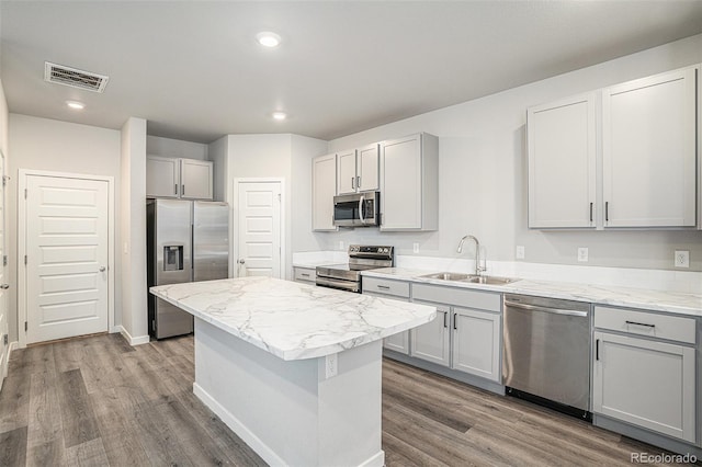 kitchen featuring gray cabinetry, sink, a center island, light stone counters, and appliances with stainless steel finishes