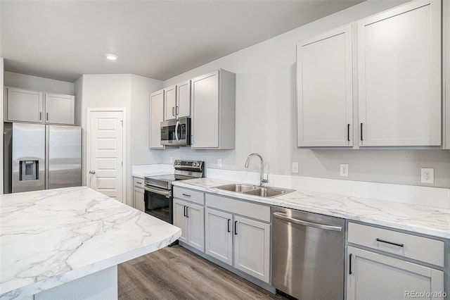 kitchen with gray cabinetry, sink, hardwood / wood-style flooring, appliances with stainless steel finishes, and light stone counters