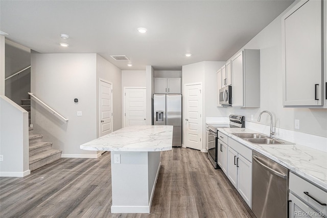 kitchen with light stone countertops, a center island, sink, stainless steel appliances, and wood-type flooring