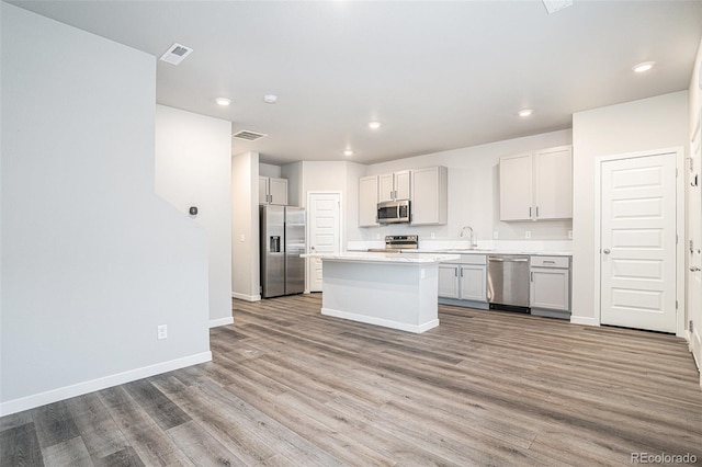 kitchen with sink, a kitchen island, light wood-type flooring, and appliances with stainless steel finishes