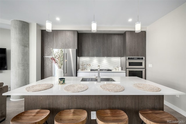 kitchen with appliances with stainless steel finishes, a breakfast bar, a kitchen island with sink, and hanging light fixtures