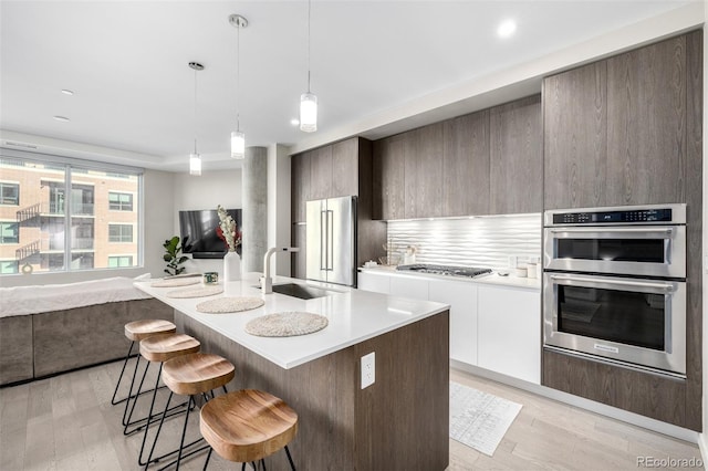 kitchen with white cabinetry, hanging light fixtures, light hardwood / wood-style flooring, appliances with stainless steel finishes, and a kitchen island with sink