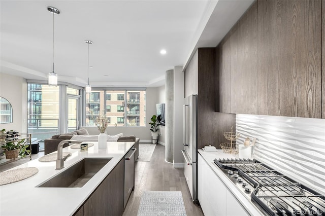 kitchen with decorative light fixtures, sink, dark brown cabinetry, stainless steel appliances, and light hardwood / wood-style flooring