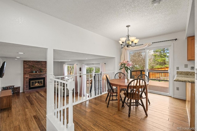dining space with wood finished floors, a brick fireplace, a textured ceiling, and a chandelier