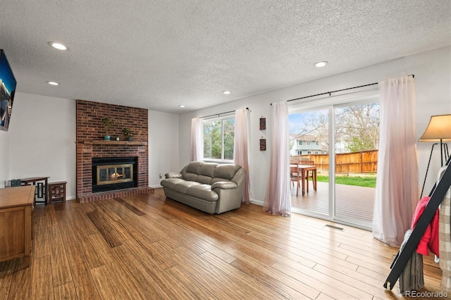 living room with visible vents, a textured ceiling, a brick fireplace, and wood finished floors