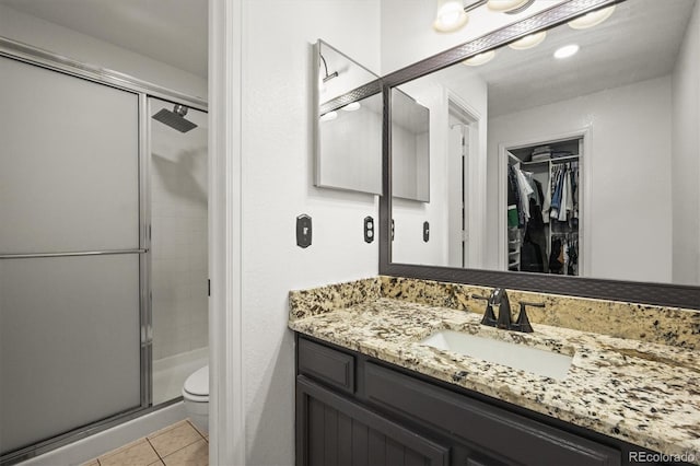 full bath featuring tile patterned flooring, a stall shower, vanity, toilet, and a spacious closet