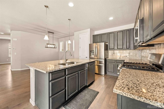 kitchen featuring tasteful backsplash, light wood-style flooring, light stone countertops, stainless steel appliances, and a sink