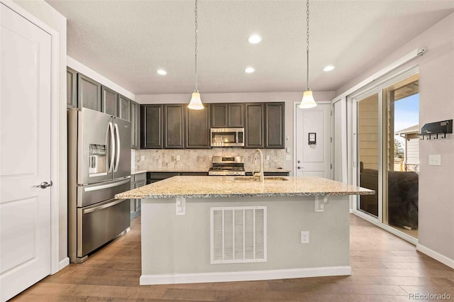 kitchen with visible vents, decorative backsplash, appliances with stainless steel finishes, light stone countertops, and a sink