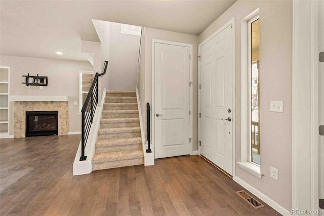 foyer entrance featuring baseboards, visible vents, dark wood finished floors, a glass covered fireplace, and stairs