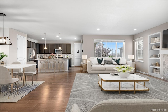 living area with dark wood-style flooring, built in shelves, and recessed lighting