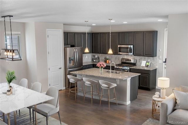 kitchen with a kitchen breakfast bar, a sink, dark wood-style flooring, tasteful backsplash, and appliances with stainless steel finishes