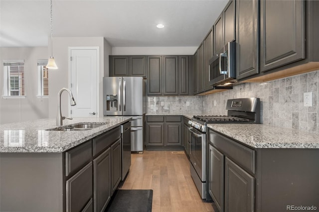 kitchen featuring tasteful backsplash, light stone countertops, appliances with stainless steel finishes, light wood finished floors, and a sink