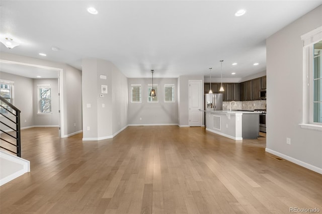 unfurnished living room with a sink, recessed lighting, stairs, and light wood finished floors