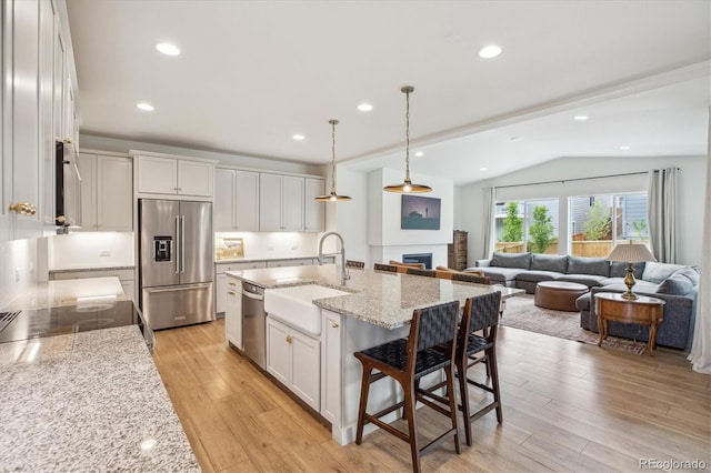 14423 Shasta Daisy Ln, Parker, CO 80134 - kitchen with appliances with stainless steel finishes, vaulted ceiling, light wood-style floors, a fireplace, and light stone countertops