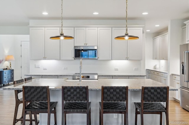 14423 Shasta Daisy Ln, Parker, CO 80134 - kitchen featuring stainless steel appliances, light wood finished floors, hanging light fixtures, light stone countertops, and a breakfast bar area