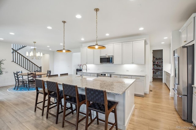 14423 Shasta Daisy Ln, Parker, CO 80134 - kitchen featuring appliances with stainless steel finishes, light wood-style floors, an island with sink, light stone counters, and recessed lighting