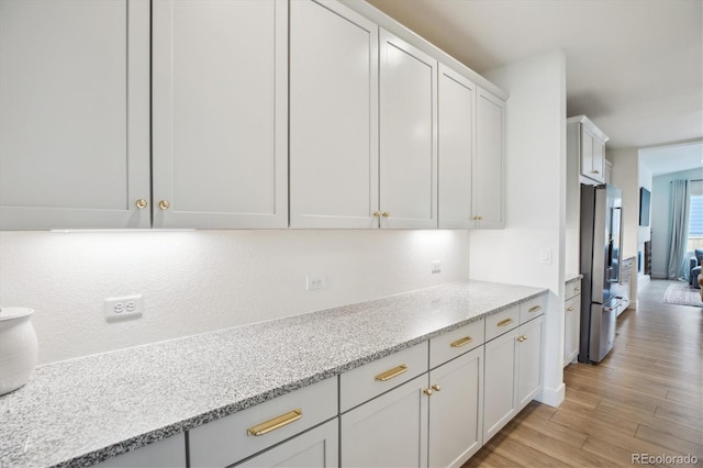 14423 Shasta Daisy Ln, Parker, CO 80134 - kitchen featuring stainless steel fridge with ice dispenser, light wood-style flooring, white cabinetry, and light stone countertops