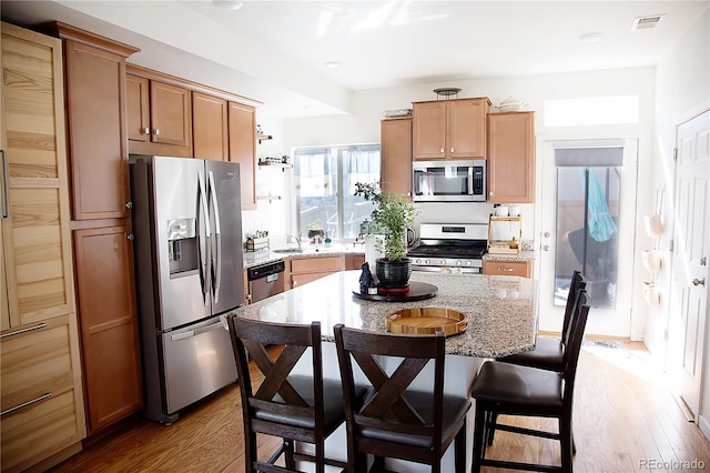 kitchen with visible vents, a kitchen island, a kitchen bar, light wood-style floors, and stainless steel appliances