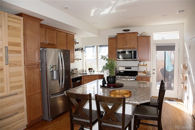 kitchen featuring light stone counters, stainless steel appliances, a kitchen island, and brown cabinetry