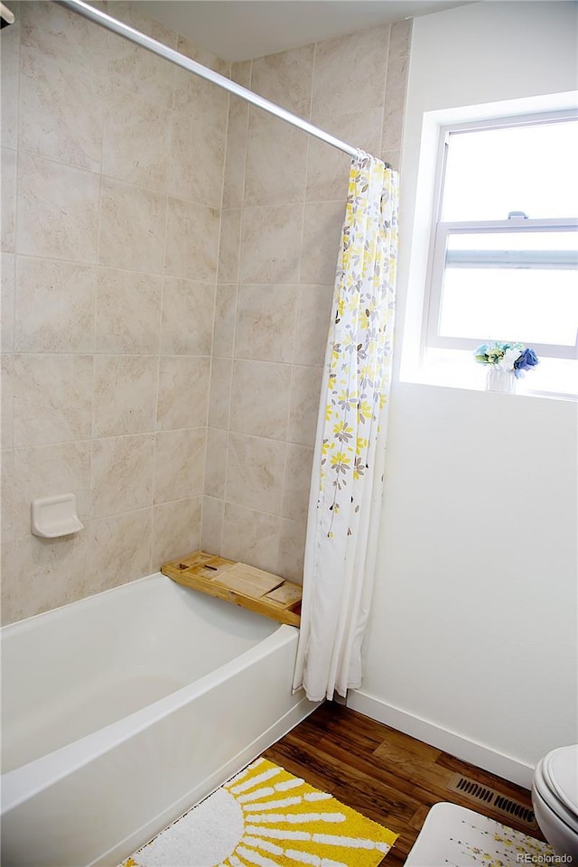 bathroom with wood finished floors, visible vents, baseboards, shower / tub combo, and toilet