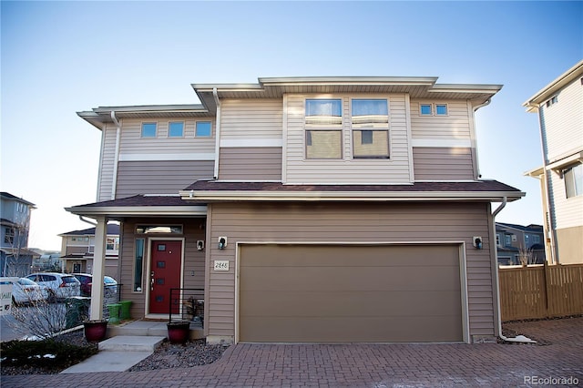 view of front of house with decorative driveway, an attached garage, and fence