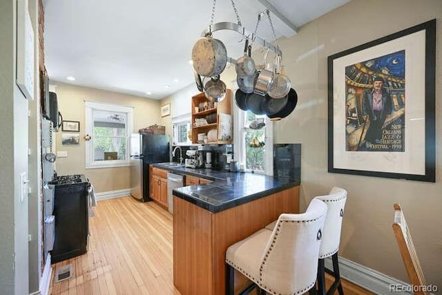 1027 S University Blvd, Denver, CO 80209 - kitchen featuring brown cabinets, light wood-style flooring, a kitchen bar, dark countertops, and appliances with stainless steel finishes