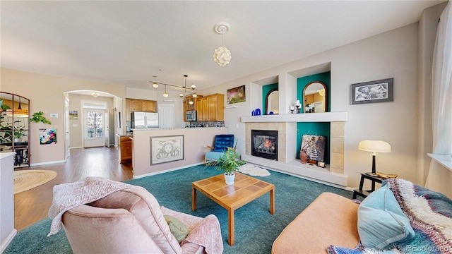 living room with baseboards, arched walkways, wood finished floors, and a tile fireplace