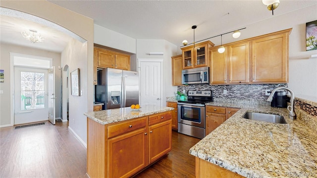 kitchen with backsplash, light stone counters, dark wood-style floors, stainless steel appliances, and a sink