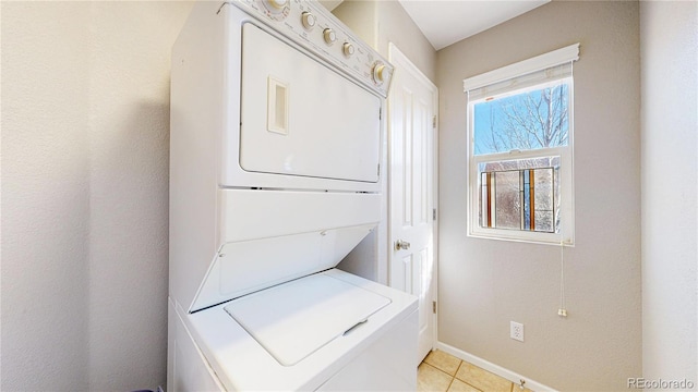 clothes washing area with baseboards, stacked washer and dryer, light tile patterned flooring, and laundry area