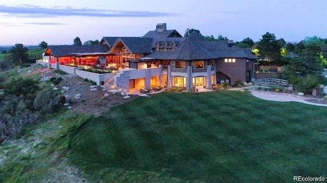 back house at dusk featuring a balcony and a yard