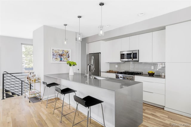 3156 W 20th Ave, Denver, CO 80211 - kitchen with appliances with stainless steel finishes, a breakfast bar, decorative backsplash, light wood-style floors, and white cabinetry