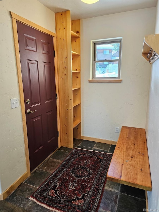 foyer entrance featuring baseboards, stone tile flooring, and a textured wall