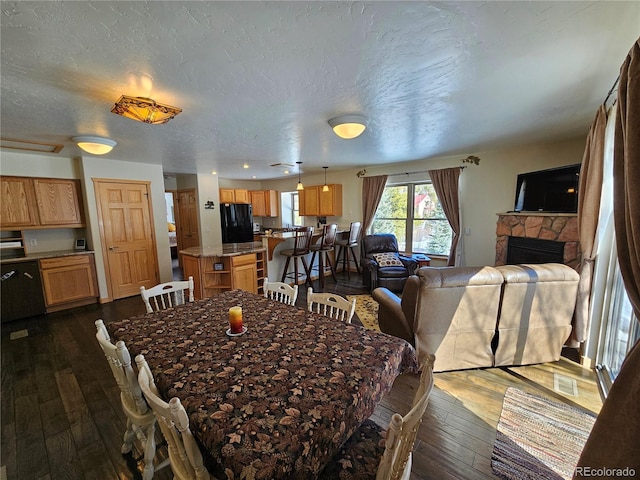 dining area featuring visible vents, dark wood finished floors, a stone fireplace, and a textured ceiling