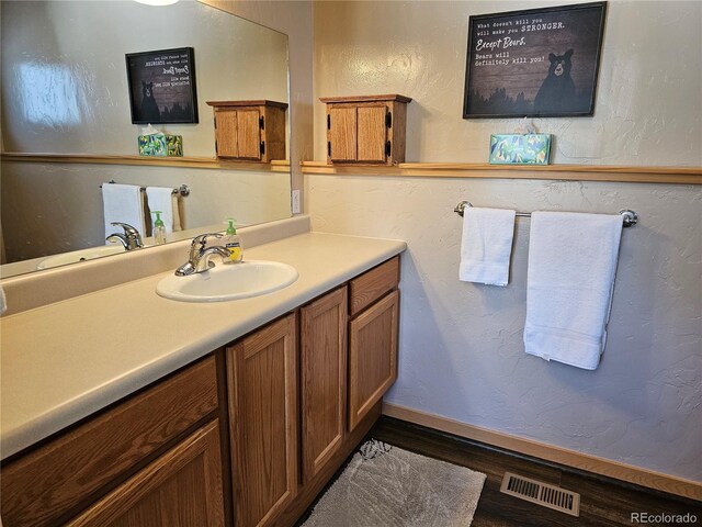 bathroom featuring a textured wall, wood finished floors, vanity, visible vents, and baseboards