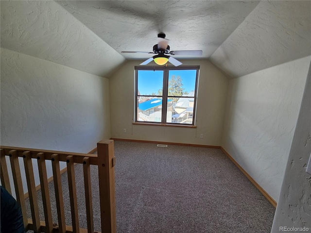 bonus room with a textured ceiling, a textured wall, carpet floors, and vaulted ceiling