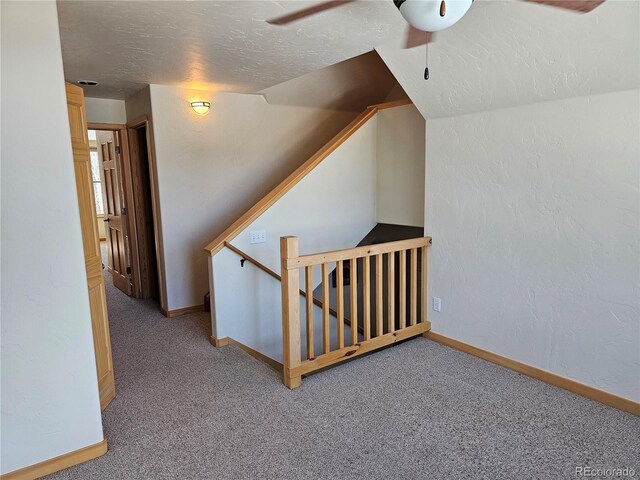 additional living space with a textured ceiling, a textured wall, carpet flooring, a ceiling fan, and baseboards