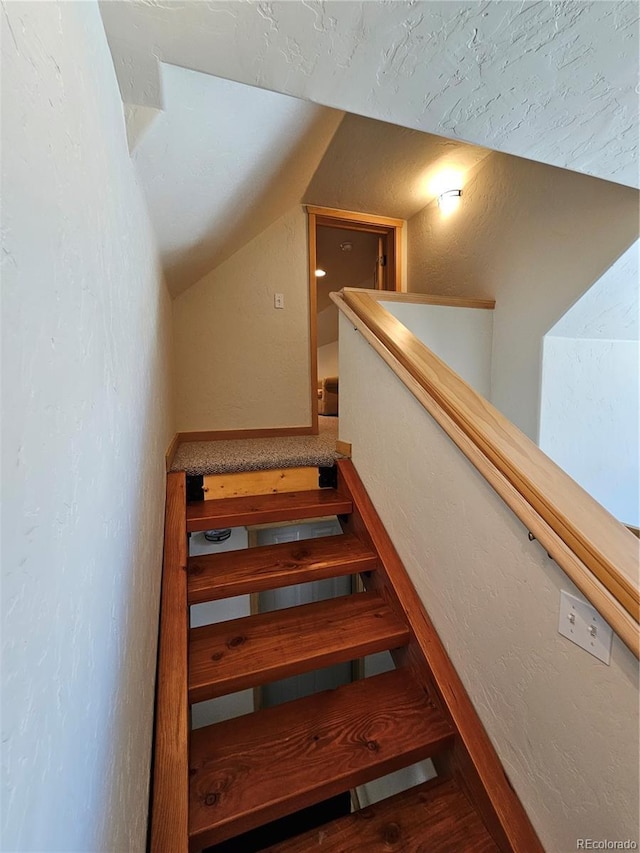 stairway with vaulted ceiling, a textured wall, and wood finished floors